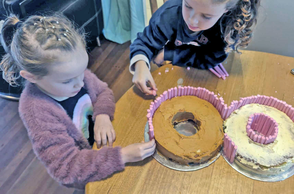 Girls sticking musk sticks onto a number eight cake